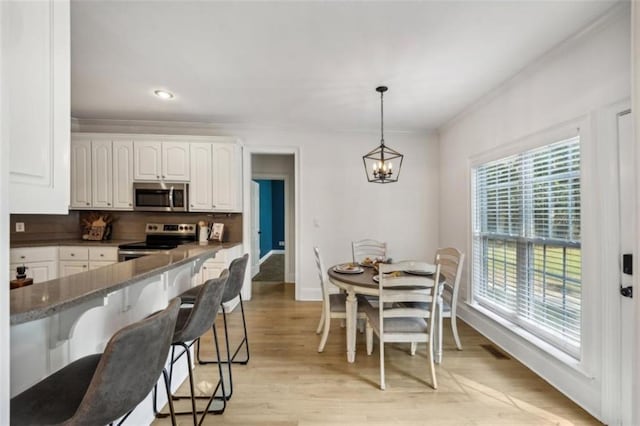 kitchen featuring stainless steel appliances, white cabinets, light wood-type flooring, tasteful backsplash, and a kitchen bar