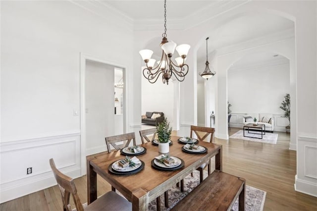 dining area with arched walkways, a decorative wall, an inviting chandelier, ornamental molding, and wood finished floors