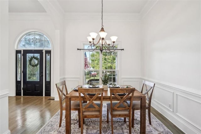 dining area with a chandelier, crown molding, wood finished floors, and a decorative wall