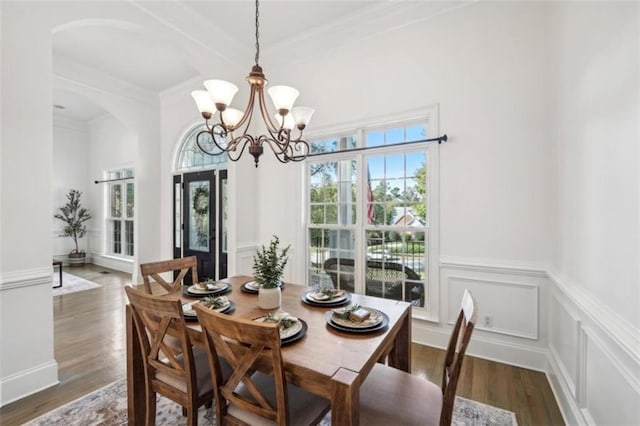 dining space featuring dark wood-style floors, arched walkways, a chandelier, and a decorative wall