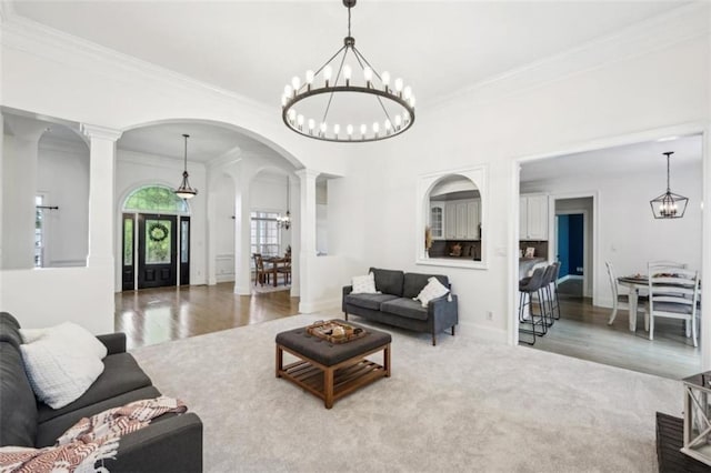 carpeted living room featuring a chandelier, arched walkways, wood finished floors, ornamental molding, and decorative columns