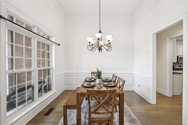 dining room featuring visible vents, ornamental molding, dark wood-type flooring, a chandelier, and a decorative wall