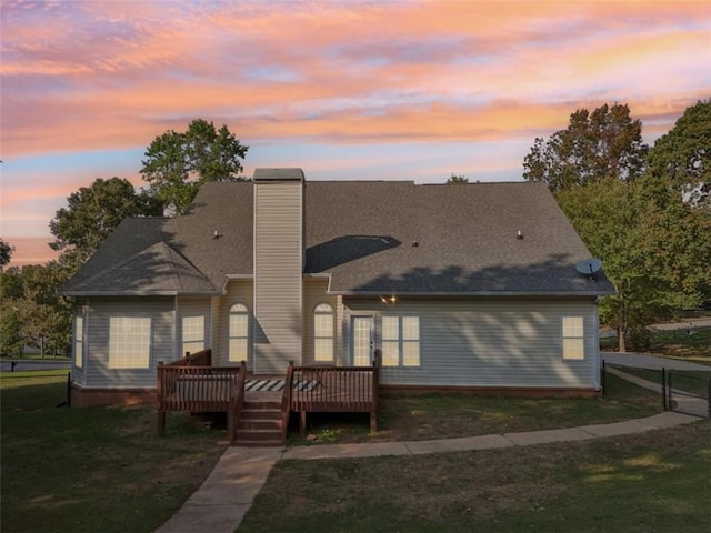 back of property at dusk featuring a deck, a yard, a chimney, and fence