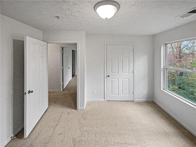 unfurnished room featuring light colored carpet, a healthy amount of sunlight, and a textured ceiling