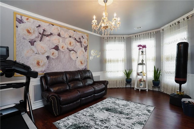 living area with crown molding, visible vents, wood finished floors, a wainscoted wall, and a chandelier