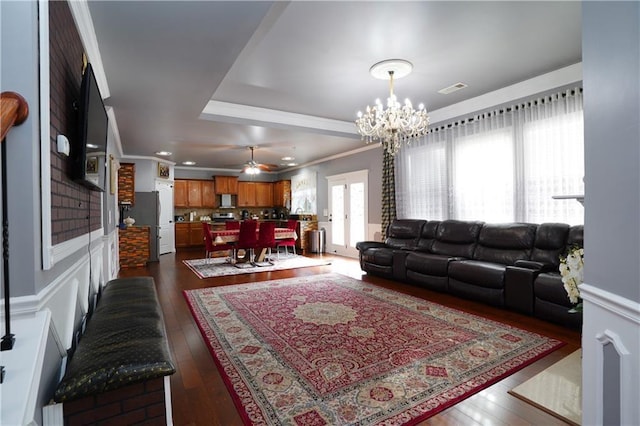 living area featuring visible vents, dark wood finished floors, ceiling fan with notable chandelier, ornamental molding, and a tray ceiling