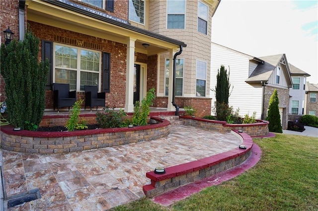 view of exterior entry with a yard, a porch, and brick siding