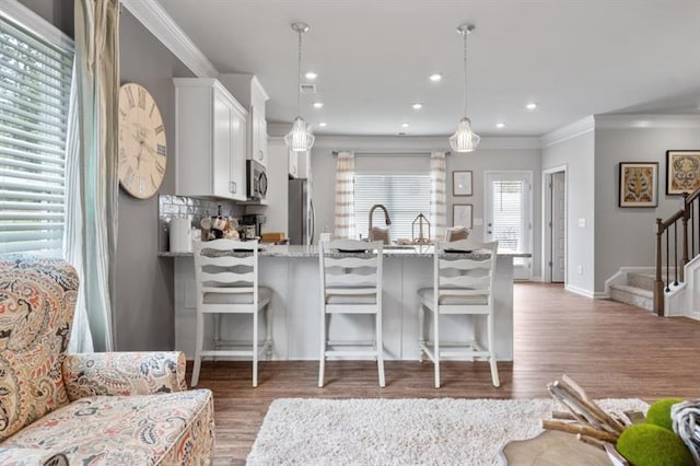 kitchen with appliances with stainless steel finishes, a peninsula, wood finished floors, white cabinetry, and crown molding