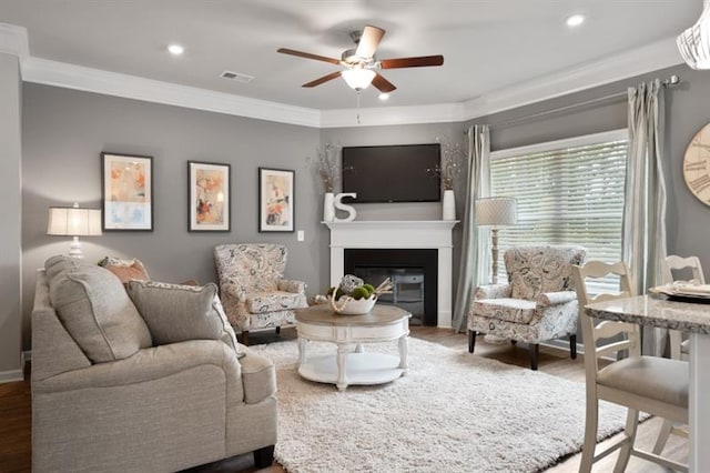 living area featuring crown molding, ceiling fan, wood finished floors, a glass covered fireplace, and recessed lighting