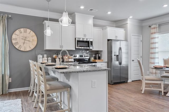 kitchen featuring appliances with stainless steel finishes, a sink, light wood finished floors, white cabinets, and a breakfast bar