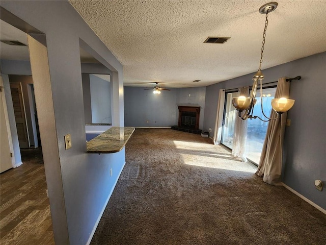 unfurnished living room with ceiling fan with notable chandelier, a textured ceiling, and dark colored carpet