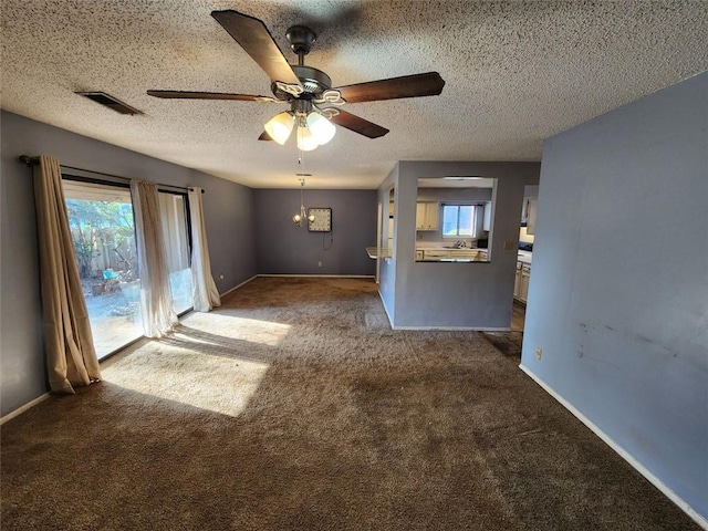 unfurnished living room featuring ceiling fan with notable chandelier, a textured ceiling, and dark colored carpet