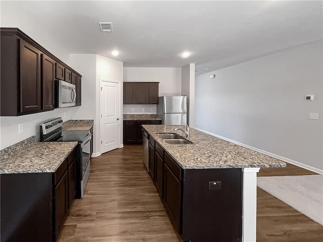 kitchen featuring a kitchen island with sink, dark wood-type flooring, sink, appliances with stainless steel finishes, and dark brown cabinetry