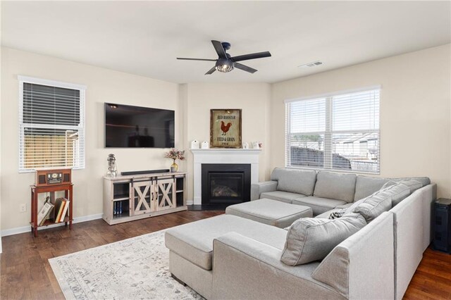 living area with a fireplace with flush hearth, baseboards, dark wood finished floors, ceiling fan, and visible vents