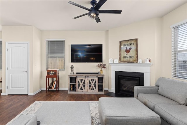 living room featuring a ceiling fan, a glass covered fireplace, baseboards, and wood finished floors