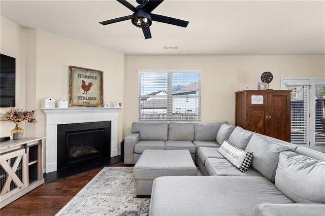 living area featuring a fireplace, visible vents, a ceiling fan, and dark wood finished floors