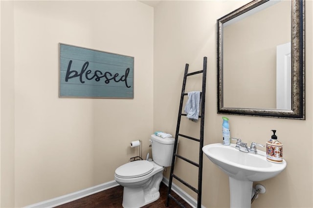 bathroom featuring baseboards, wood finished floors, toilet, and a sink