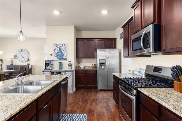kitchen with a sink, pendant lighting, light stone countertops, stainless steel appliances, and dark wood-type flooring