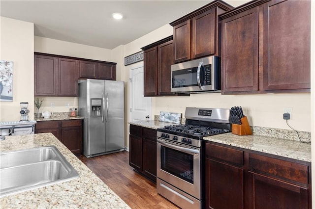 kitchen with dark wood finished floors, a sink, light stone counters, dark brown cabinets, and appliances with stainless steel finishes