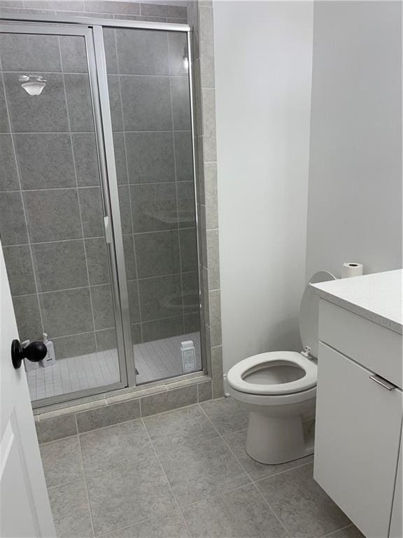 bathroom with tile patterned flooring, vanity, a shower with shower door, and toilet