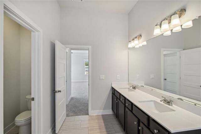 full bathroom featuring toilet, double vanity, and baseboards