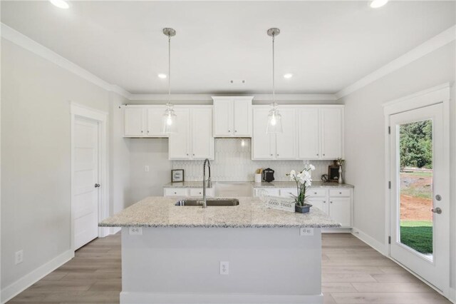 kitchen with a sink, white cabinets, an island with sink, tasteful backsplash, and light wood finished floors