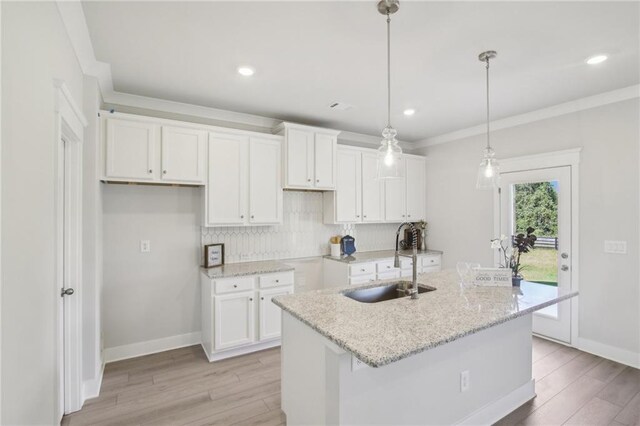kitchen with a sink, white cabinetry, light wood finished floors, backsplash, and crown molding