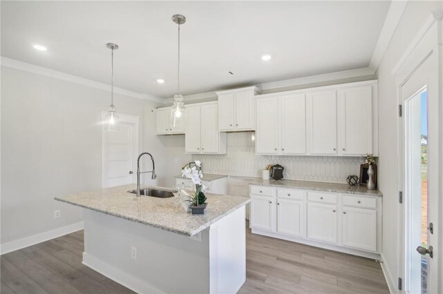 kitchen with a sink, decorative backsplash, white cabinetry, a kitchen island with sink, and crown molding