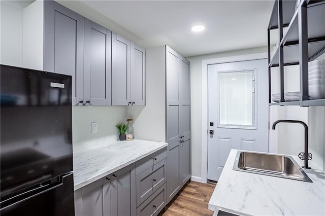 kitchen featuring freestanding refrigerator, light wood-type flooring, recessed lighting, a sink, and gray cabinetry