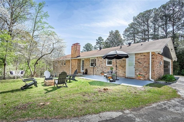 back of house with an outdoor fire pit, brick siding, a chimney, a patio, and a yard