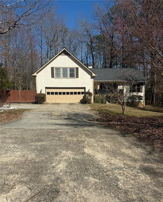 view of property exterior with driveway, an attached garage, and fence