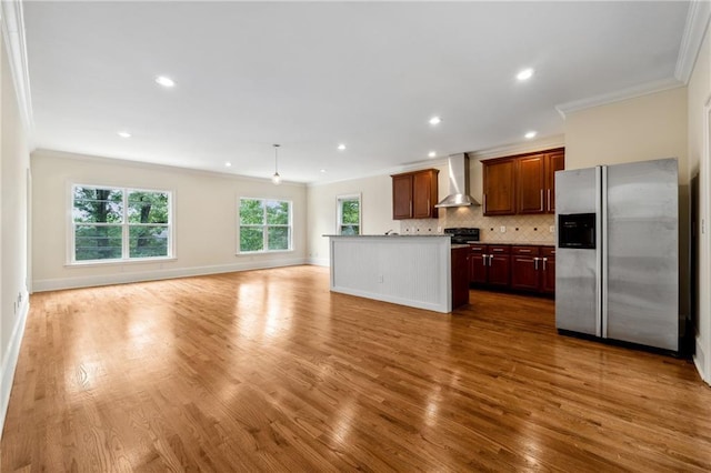 kitchen with decorative backsplash, stainless steel fridge with ice dispenser, wall chimney exhaust hood, open floor plan, and crown molding