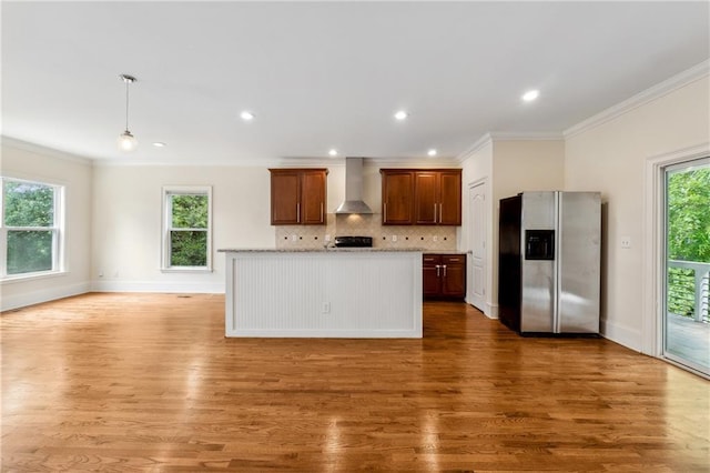 kitchen with stainless steel fridge, wall chimney exhaust hood, ornamental molding, wood finished floors, and backsplash