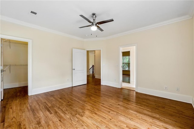 unfurnished bedroom with light wood-style floors, a walk in closet, visible vents, and crown molding