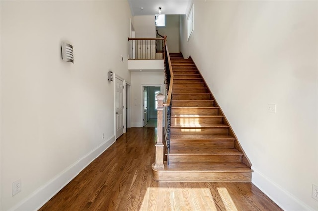 stairway with a towering ceiling, a healthy amount of sunlight, baseboards, and wood finished floors