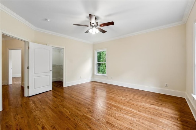 unfurnished bedroom with crown molding, baseboards, a walk in closet, and wood finished floors