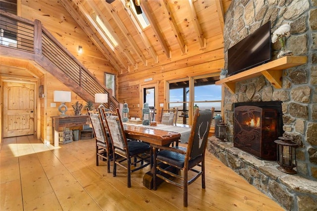 dining room with wood walls, wood ceiling, high vaulted ceiling, a fireplace, and light hardwood / wood-style floors