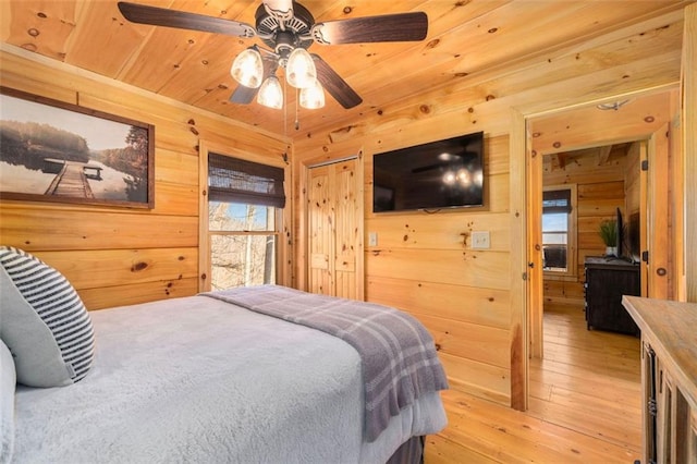 bedroom with ceiling fan, wooden ceiling, light hardwood / wood-style floors, and wood walls