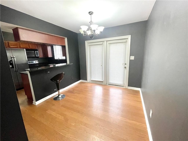 kitchen featuring an inviting chandelier, a kitchen breakfast bar, hanging light fixtures, stainless steel appliances, and light wood-type flooring