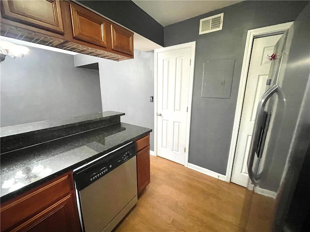 kitchen with appliances with stainless steel finishes, electric panel, light hardwood / wood-style floors, and dark stone counters