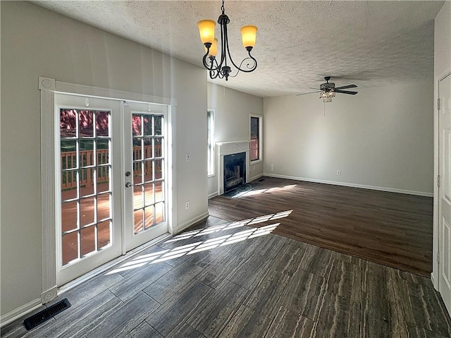 unfurnished living room featuring french doors, dark hardwood / wood-style floors, a textured ceiling, and ceiling fan with notable chandelier