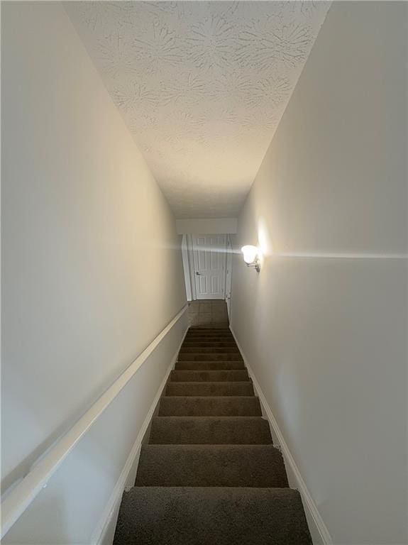 stairway with a textured ceiling and carpet floors