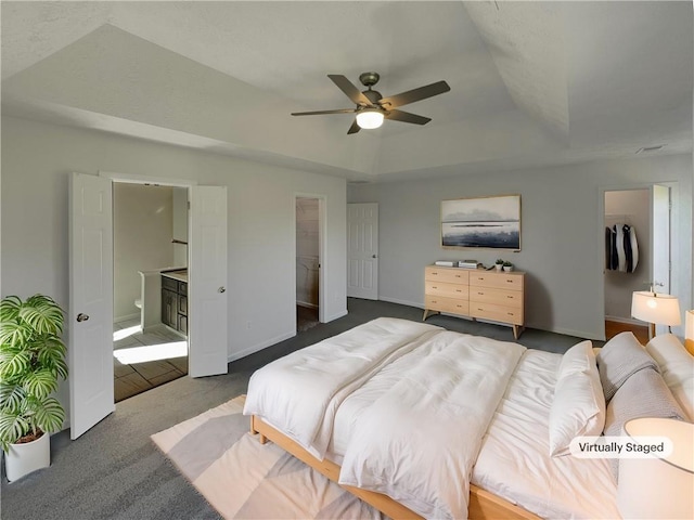 carpeted bedroom featuring a walk in closet, ceiling fan, a tray ceiling, connected bathroom, and a closet