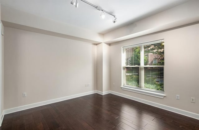 spare room featuring rail lighting, dark wood finished floors, and baseboards