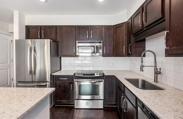 kitchen with tasteful backsplash, appliances with stainless steel finishes, dark wood-type flooring, a sink, and dark brown cabinetry