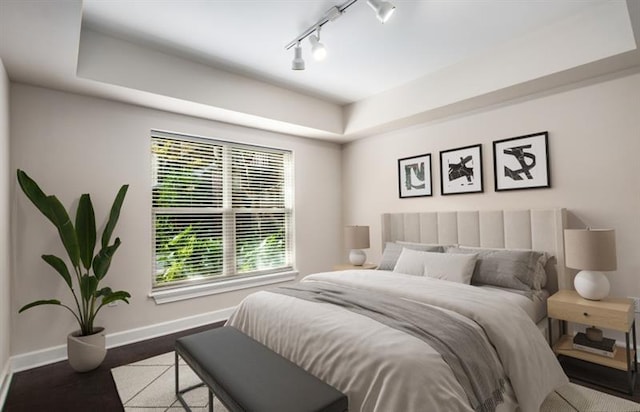 bedroom featuring a tray ceiling, track lighting, wood finished floors, and baseboards