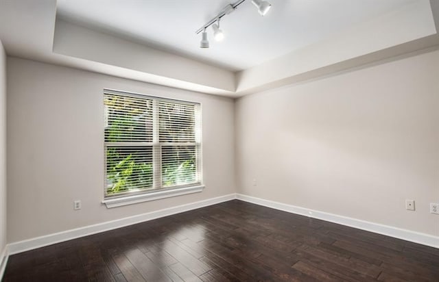 empty room with dark wood-style flooring, a raised ceiling, rail lighting, and baseboards