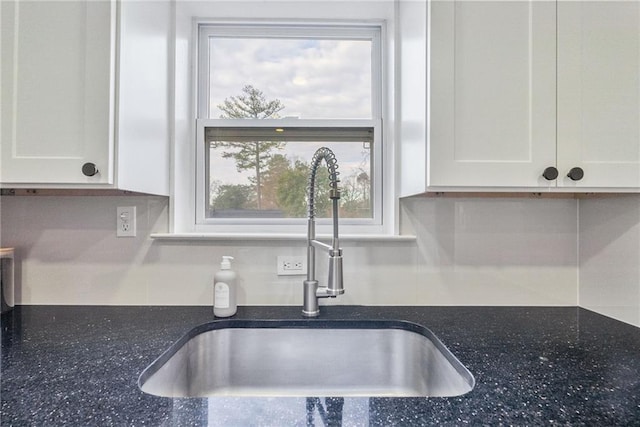 details with a sink, dark stone counters, decorative backsplash, and white cabinetry