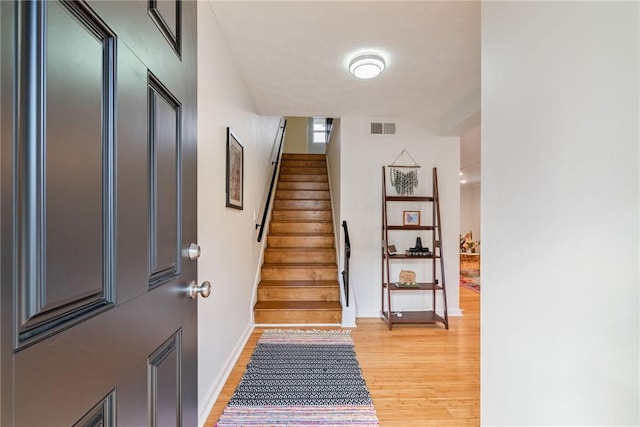 foyer with stairway, baseboards, light wood-type flooring, and visible vents
