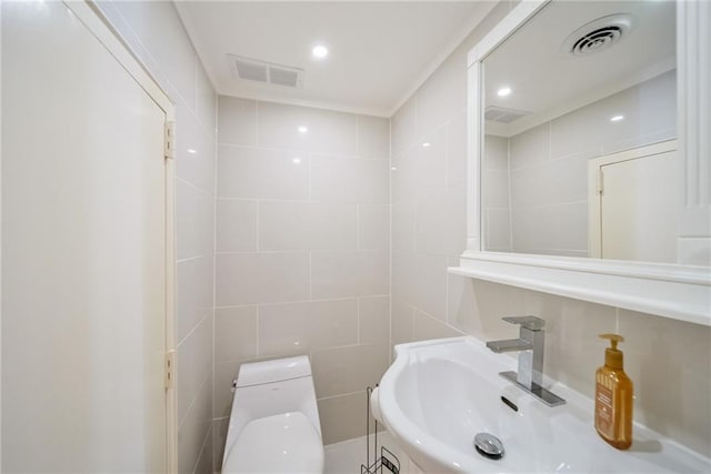 half bath with a sink, tile walls, toilet, and visible vents